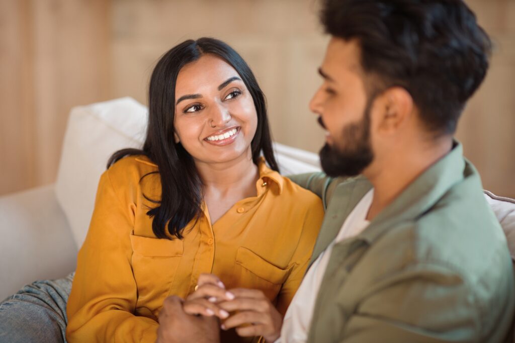 Loving indian couple holding hands and talking, enjoying pleasant conversation starters and flirt, sitting on