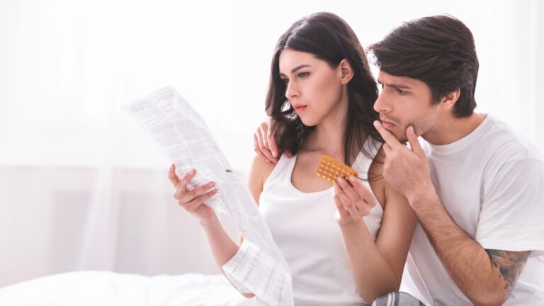 Young Couple Reading Instructions for Birth Control Pills in Bed